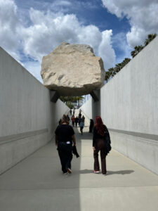 Über einem mit Mauern umsäumten Fußgängerweg liegt ein großer Gesteinsbrocken, Landart von Michael Heizer